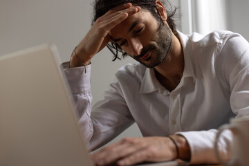 portrait d'un jeune employé de bureau assis devant son ordinateur. Il est fatigué et stressé et...