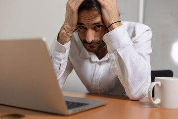 portrait d'un jeune employé de bureau assis devant son ordinateur. Il est fatigué et stressé et...