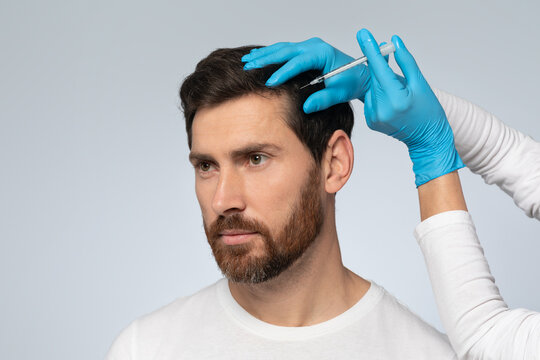 Middle aged man getting hair treatment at beauty salon, having mesotherapy session, grey background