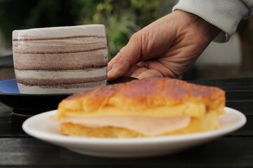 Persona poniendo un café y una medialuna sobre una mesa