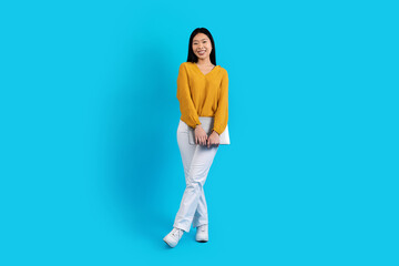 Fototapeta na wymiar Happy young asian woman with laptop posing on blue