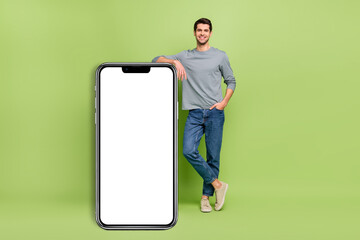 Full length photo of cheerful male lean on new smartphone model promotion ad isolated on green color background