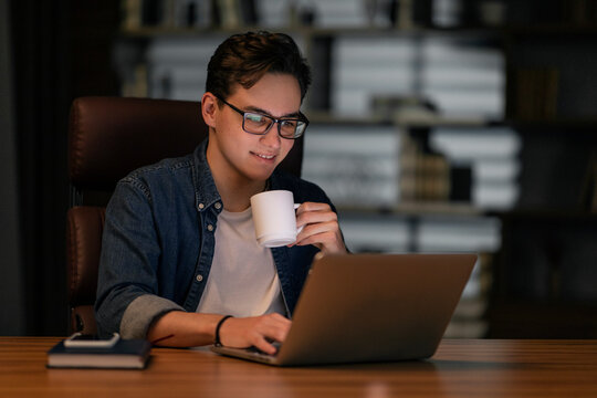 Overworked young man drinking coffee while working late at night