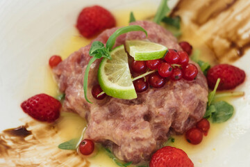 Delicious meat lovers' dish - dry aged beef tartare with anchovy, capers, lime, soy sauce, red currant and fresh strawberry