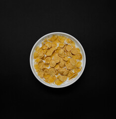 Corn flakes with milk in white plate isolated on black background. Top view, copy space.