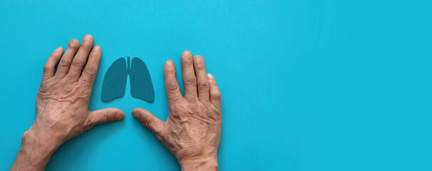 hands of a pensioner and the symbol of the organ lungs on a blue background, banner, copyspace . the concept of lung health, the harm of smoking,treatment of covid, defeat of the disease lung cancer