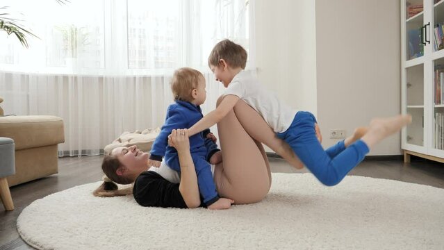 Funny shot of mother with two sons lying on floor and doing fitness exercises and stretching. Family healthcare, active lifestyle, parenting and child development.
