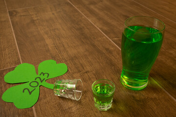shot and pint glasses on wooden bar background filled with green spirit cocktail and shamrock,...