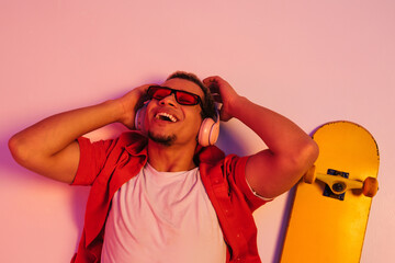 Cheerful african guy laying with skateboard isolated over gradient neon studio background