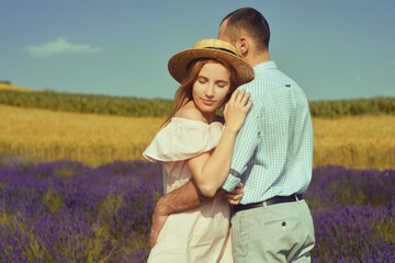 A couple in love in a field of lavender at sunset in good weather. Beautiful woman in a dress and straw panama with a man on the background of nature, love and feelings. Blue, purple lavender.