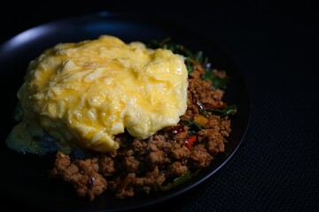 Close up Stir-fried basil with minced pork and scrambled eggs in a black plate on a black background.