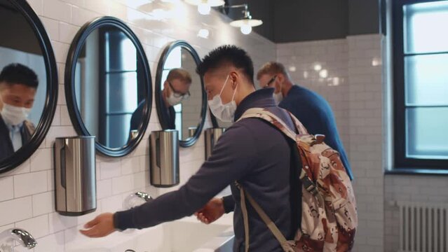 Male students in safety mask use university bathroom washing hands. Realtime