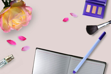 Feminine workspace: blank open notepad, pen, cosmetic accessories. Pink rose and petals on pink background. Top view.