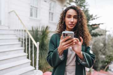 Beautiful young woman in green coat using her cellphone in the city