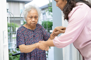 Caregiver help and support Asian senior woman while walking, stepping up to the door of the house.