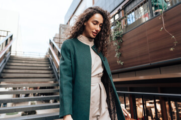 Portrait of young woman in green coat with curly hair in the city