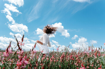 Back view of woman in long white dress in flower field holding dress with hand