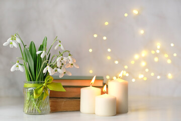 Bouquet of Snowdrop flowers , books and candles on table, abstract blurred light background. symbol of spring season. Relaxation, reading time, harmony of nature.