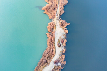 White sand and pale grass island between blue and turquoise sea or lake water