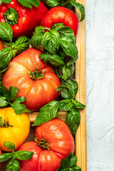box of fresh, organically homegrown vegetables tomatoes, peppers and basil on a light background. vertical image. top view. place for text