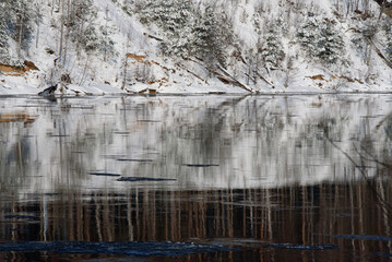 snow-covered trees in a nature park on the bank of a river where pieces of ice float in the water