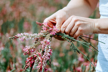 Hands of woman braiding pink flower crown