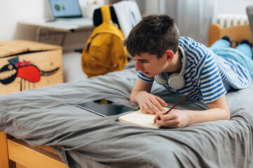 Teenage boy is doing his homework on the bed