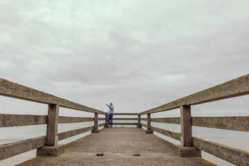 Fototapeta premium two girls are standing in jackets on a bridge in the distance and taking pictures on the phone, there is a place for an inscription beautiful sea landscape