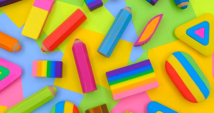 various shapes and colors of erasers arranged on a rotating table with multicolored paper sticky notes on background