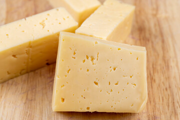 Hard cheese with holes cut into thick pieces on a cutting board