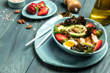 Ketogenic low carbs diet, Plate with keto foods: two eggs, avocado, grilled chicken fillet, nuts, strawberries and fresh salad. Healthy fats, clean eating for weight loss. top view