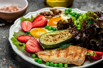 Keto breakfast two eggs, avocado, strawberry, grilled chicken fillet, nuts and fresh salad, Ketogenic diet. Plate with keto diet food. Healthy food concept, top view