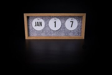 A wooden calendar block showing the date January 17th on a dark black background on a dark black background, save the date or date of event concept