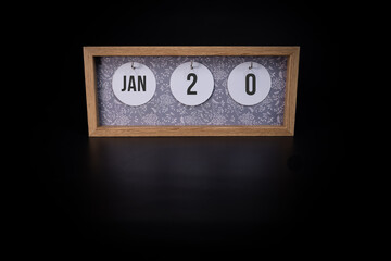 A wooden calendar block showing the date January 20th on a dark black background, save the date or date of event concept