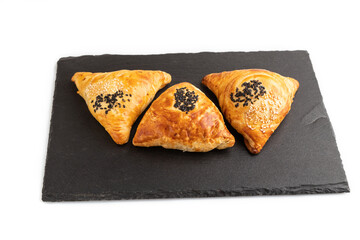 Homemade asian pastry samosa on black slate board isolated on white. side view.