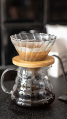 Alternative coffee brewing method, pour-over, glass teapot with freshly brewed coffee on dark background, wooden details. Close up of coffee brewing gadgets, v60