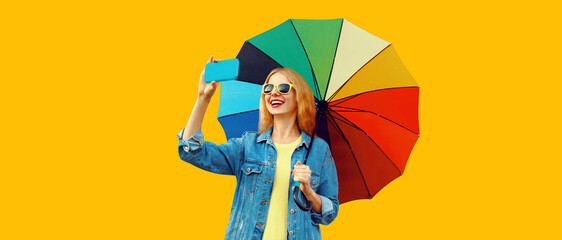 Portrait of happy smiling young woman taking selfie by smartphone with colorful umbrella isolated...
