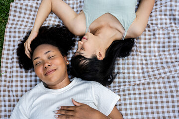 Closeup picture of happy multi ethnic Asian African girlfriends relaxing head to head sleep on grass smiling.