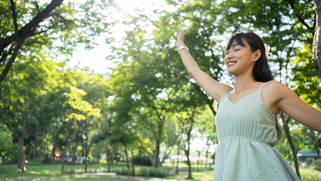 Portrait image of a happy Asian woman with arms rising in the park.