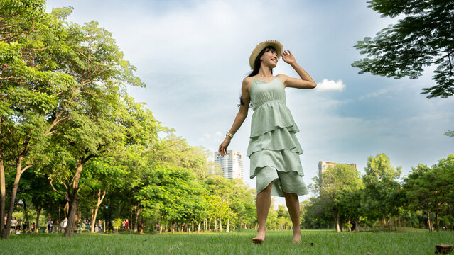 Asian girl dressed in a retro-style run with bare foot in the park. She looked on sky. She in a really good mood rising hand.