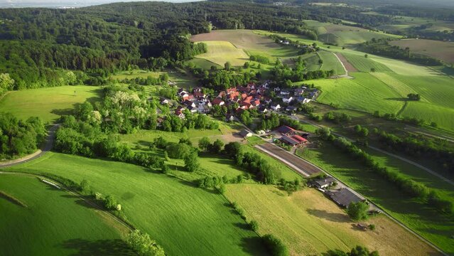 Aerial footage of an idyllic small German village surrounded with beautiful green fields, forest and meadows on hills

