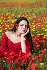 Naklejka premium Portrait of a young woman dressed in red smiling in the field of red poppies in spring. Springtime blooming season