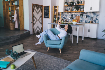 Woman using smartphone while sitting on armchair near coffee table with laptop