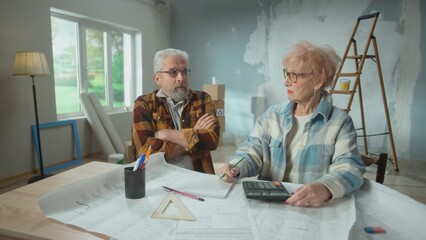 Elderly man and woman are calculating expenses of repairing an apartment on calculator. Aged couple...