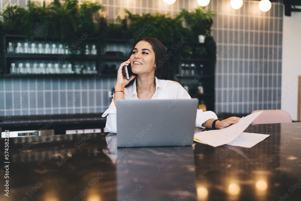 Poster smiling worker speaking on phone working with document and netbook