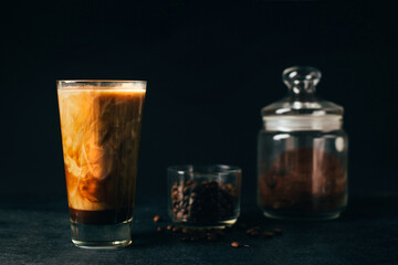 .close-up of a glass of latte coffee against the background of a glass of coffee beans and a jar of ground coffee on a black background