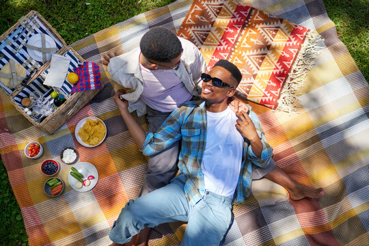 Young gay male couple cuddling, enjoying picnic on blanket in park
