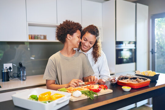 Happy, affectionate lesbian couple cooking fresh vegetables in kitchen