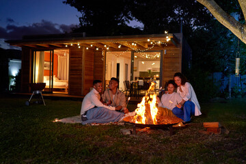 Happy gay couples roasting marshmallows at fire pit in summer backyard