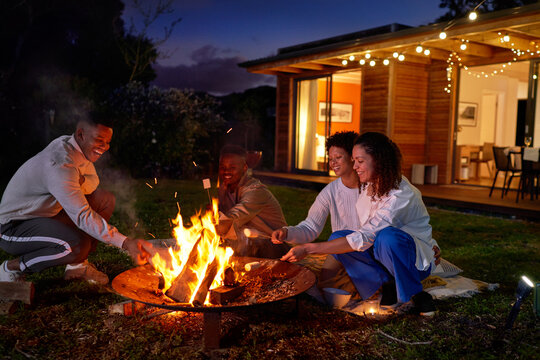 Happy gay couples roasting marshmallows at fire pit at night